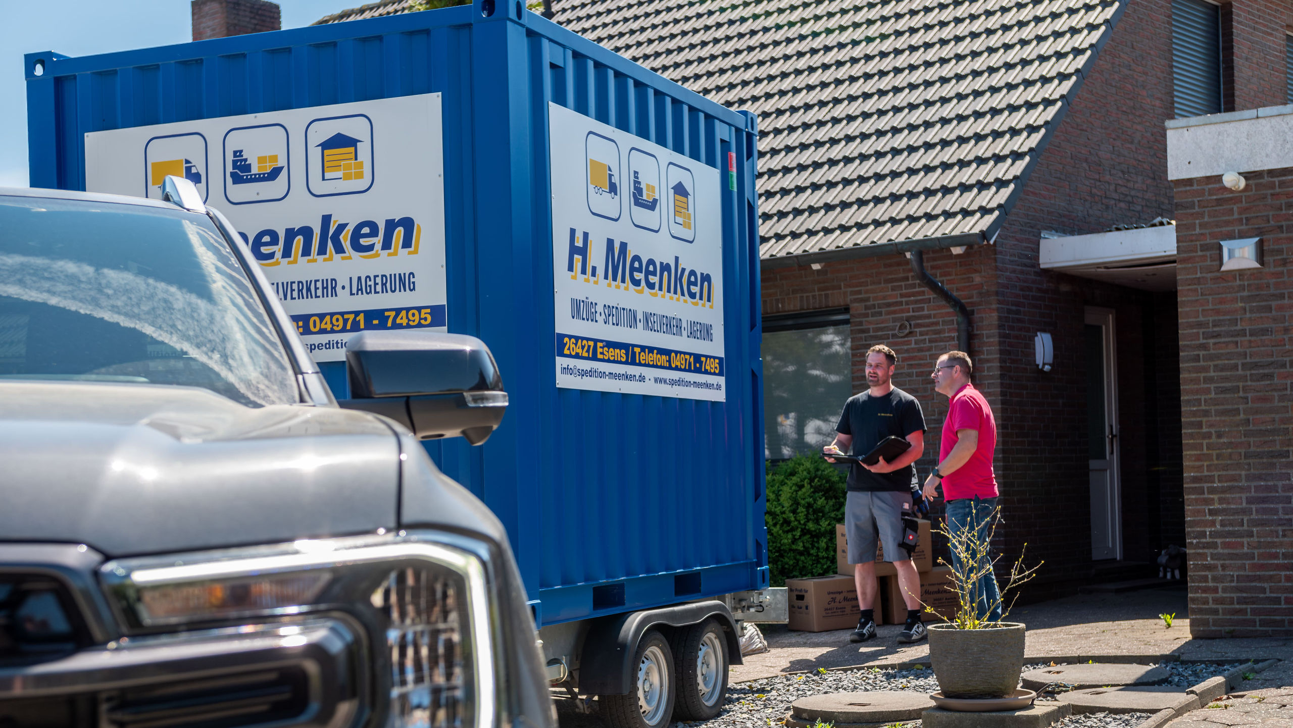Anhänger mit blauem Container steht beim Kunden in der Einfahrt und er wird mit Kartons beladen