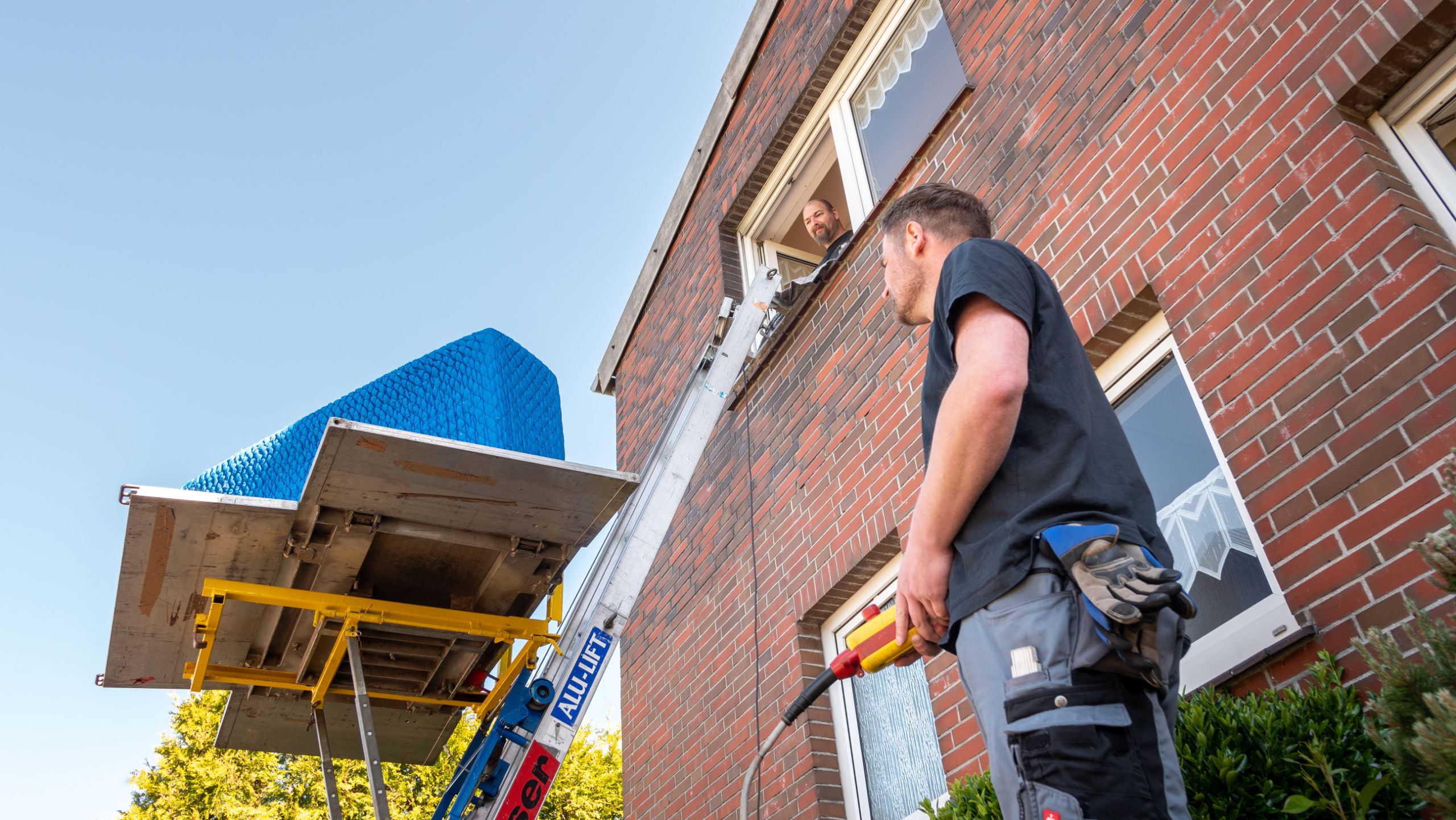 Mitarbeiter steuert per Bedienung einen Leiterlift am Fenster mit Möbelstück darauf