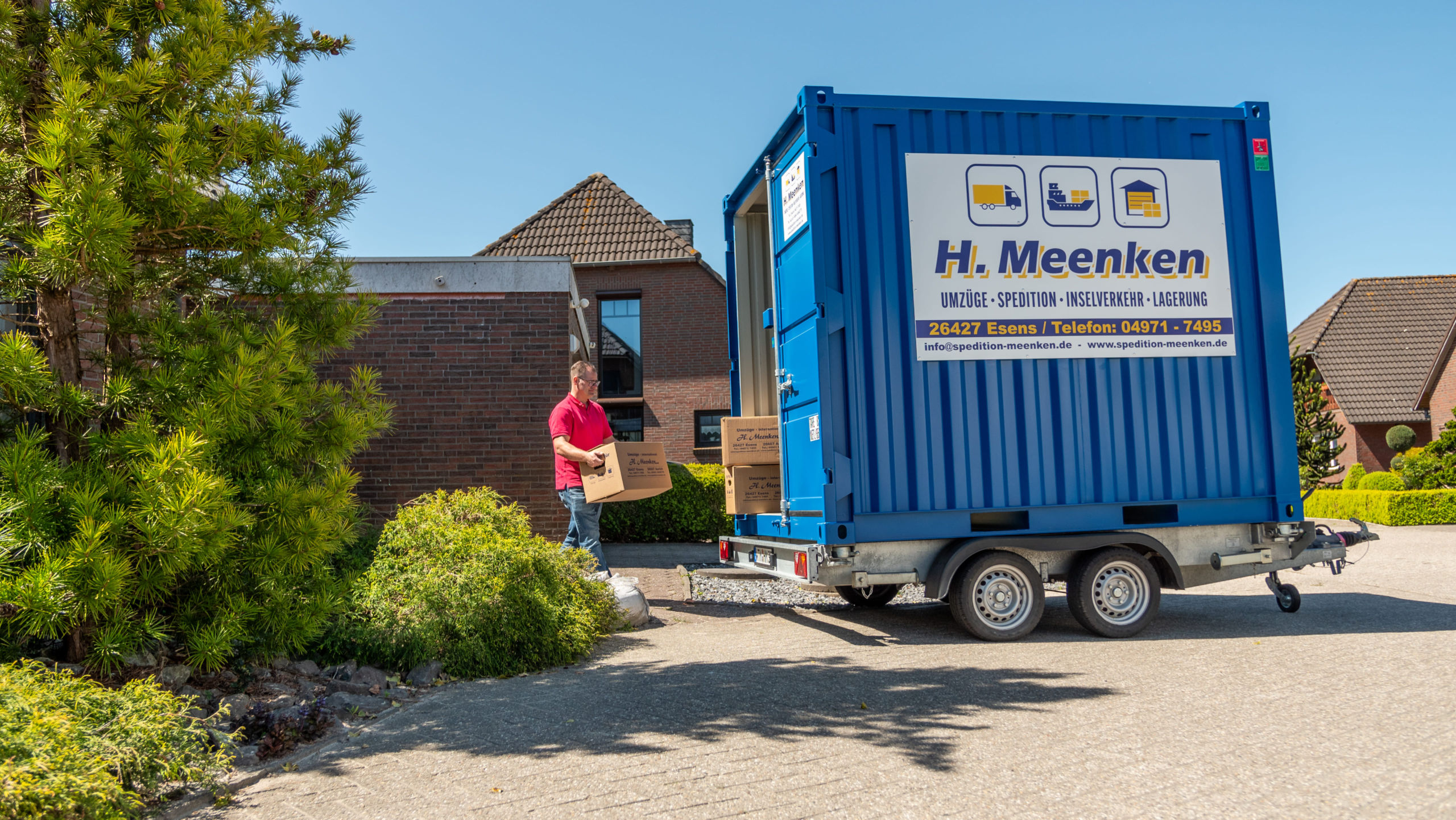 Anhänger mit Container steht vor dem Haus des Kunden und wird von Kunden mit Kartons beladen