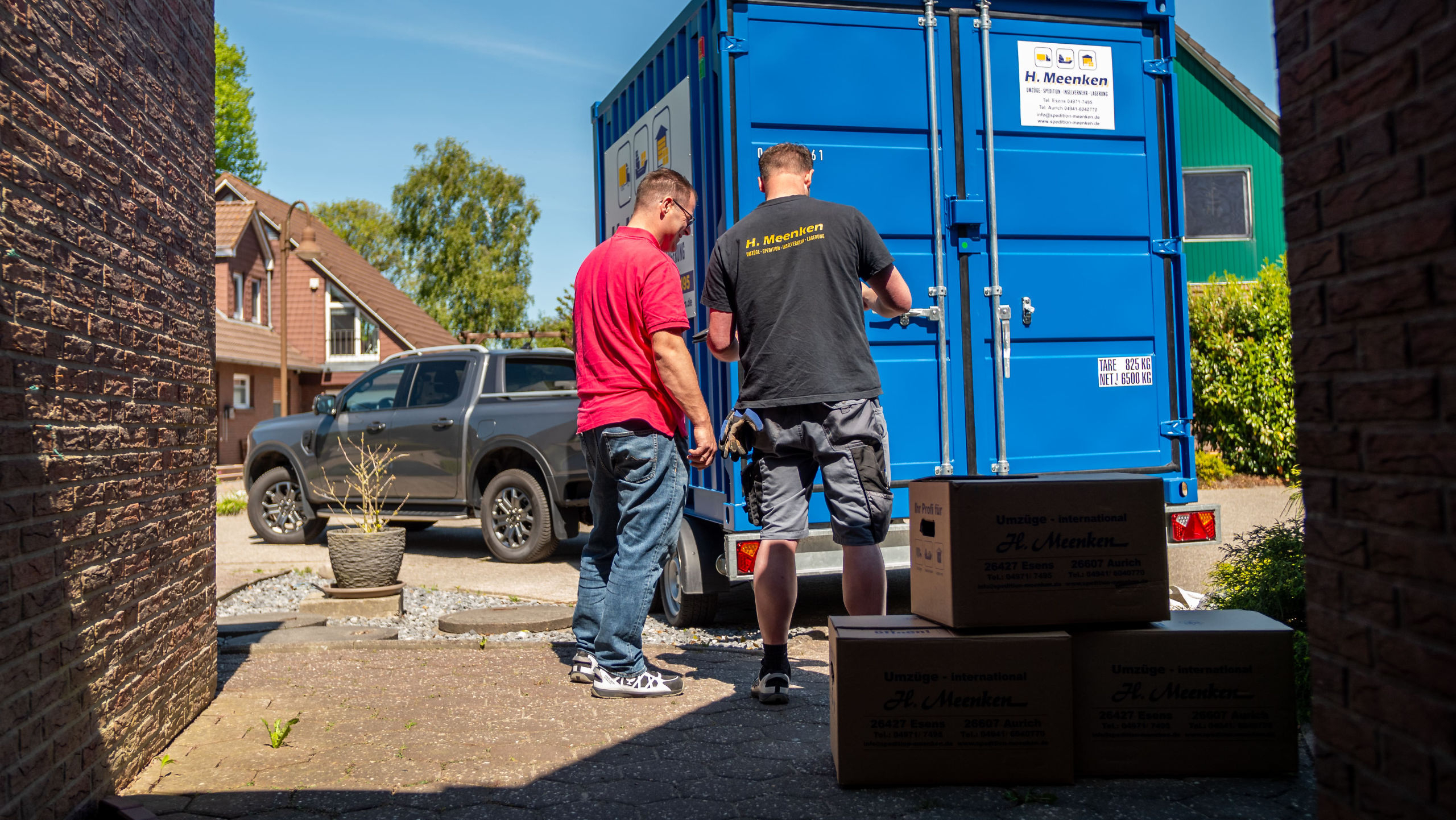 Anhänger mit blauem Container steht beim Kunden in der Einfahrt und er wird mit Kartons beladen