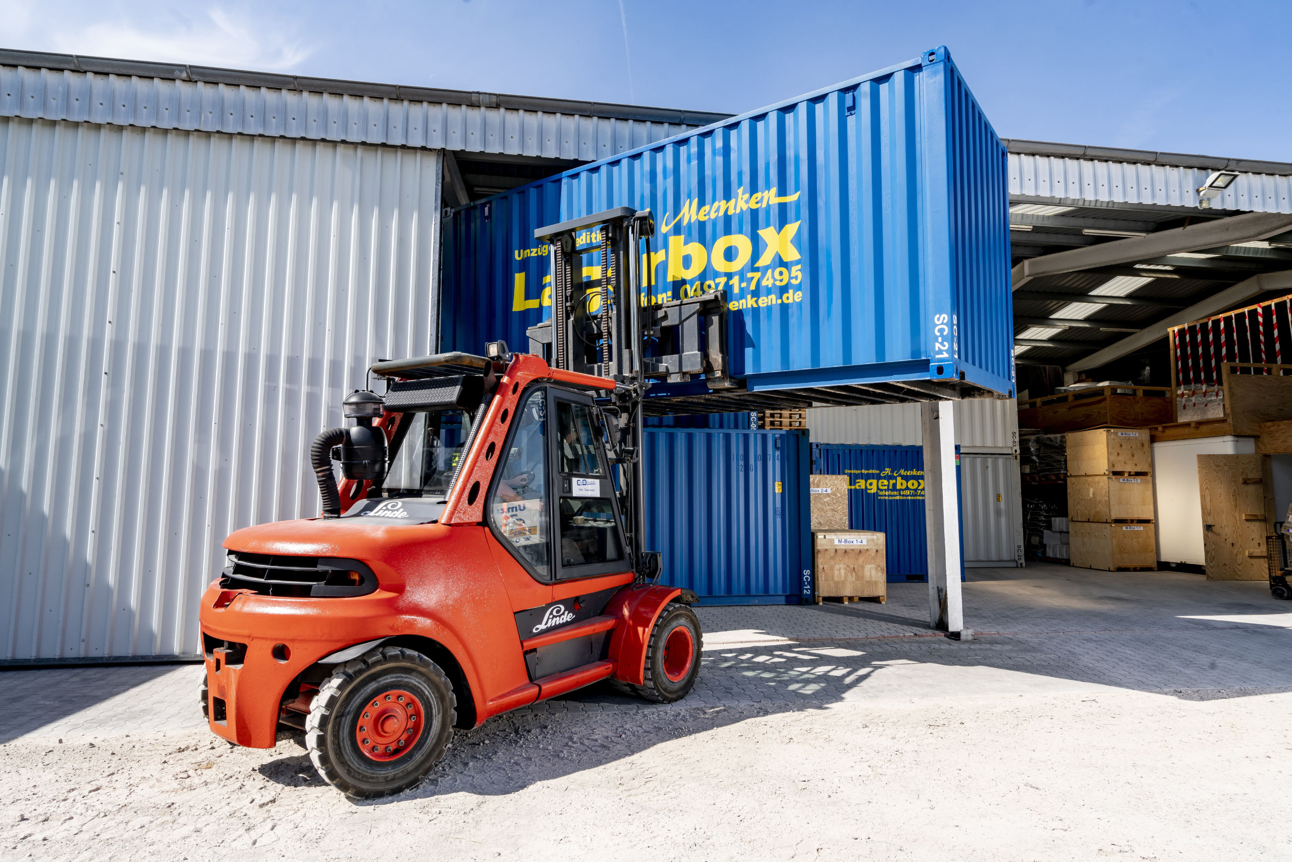 Gabelstapler hebt einen blauen Seecontainer auf einen anderen im Lagerhaus