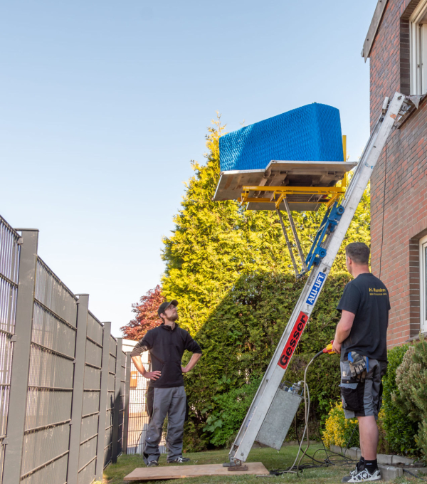 Mitarbeiter steuert per Bedienung einen Leiterlift am Fenster mit Möbelstück darauf